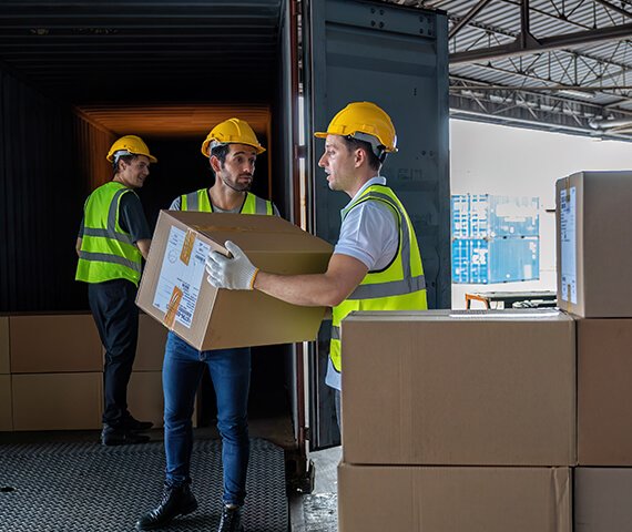 Logistics workers loading large cardboard boxes into a container RGC Shipping.